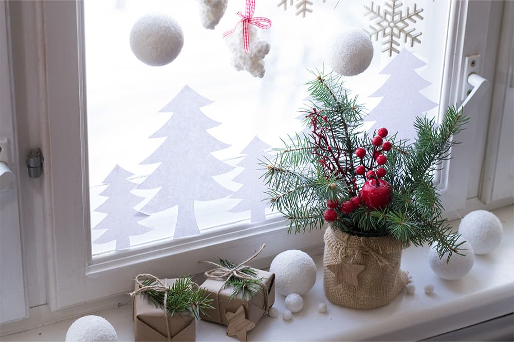 Ablakpárkány dekor: fenyőág bogyóval, becsomagolt ajándék és papírfák az ablakon