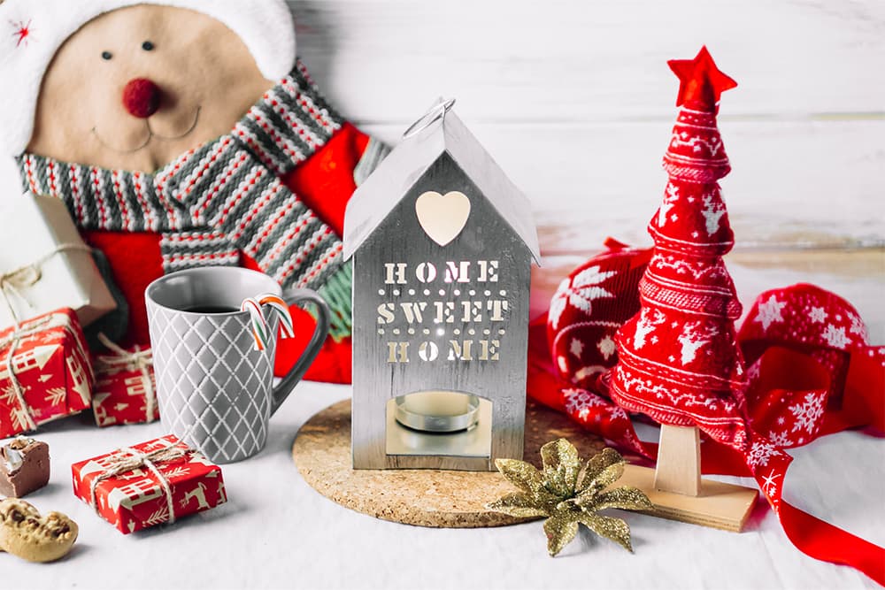 Stílusos karácsonyi dekoráció asztalon: kis házikó "Home Sweet Home" felirattal, szürke bögre, piros-fehér díszek