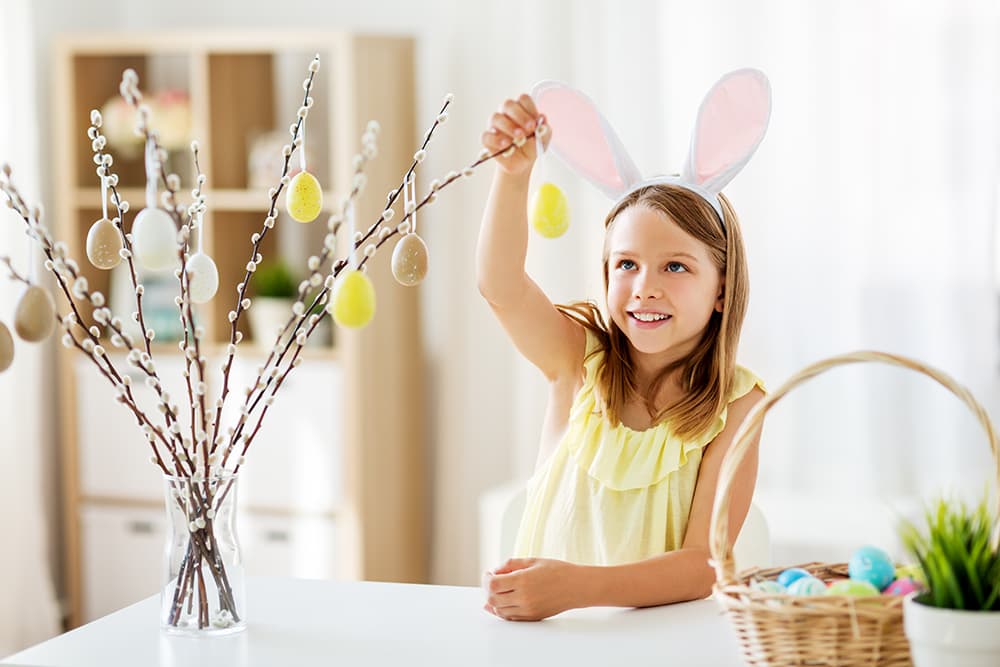 Kislány nyuszifülben barkaágat díszít húsvéti tojásokkal világos, otthonos enteriőrben